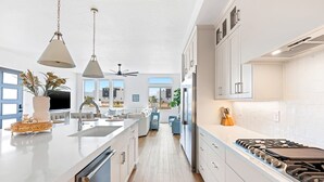 A modern kitchen with a large island, stainless steel appliances, and a view to the living area. - Beachcomber Bliss 8 Bedroom Townhouse (St. George)