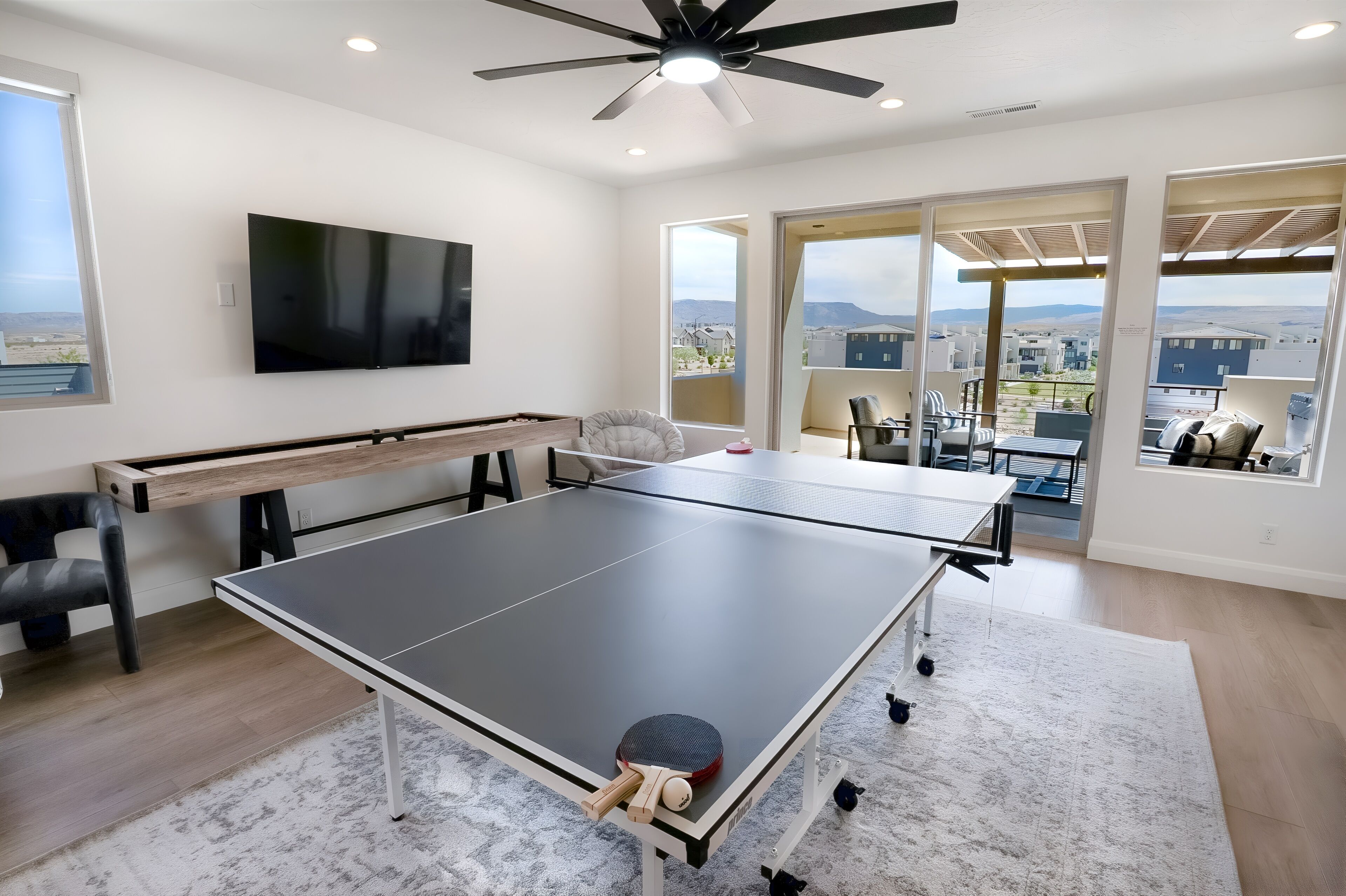 Una habitación amplia con una mesa de ping pong, un televisor de pantalla plana grande y un ventilador de techo.