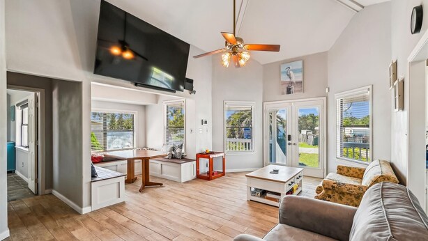 A spacious living area with a wooden floor, a ceiling fan, a flat-screen TV, a dining table, and a sofa.