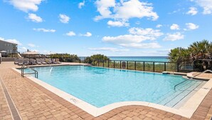 Una piscina rectangular con un cielo azul despejado y nubes al fondo.