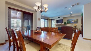 A dining area with a wooden table, chairs, a chandelier, and a television mounted on the wall. - Woodwinds #1303 4 Bedroom Condo by RedAwning (Mammoth Lakes)