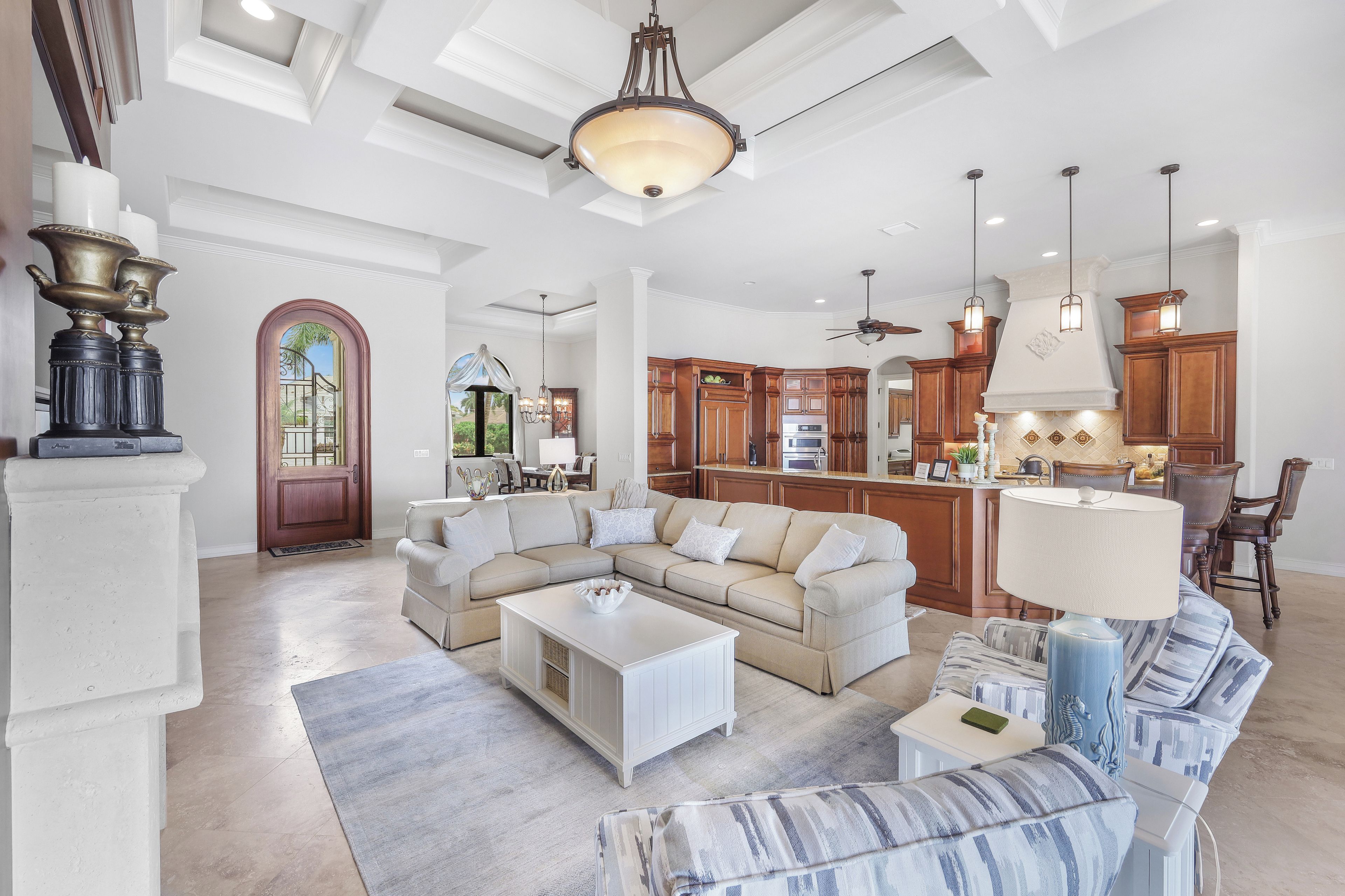 A spacious living room with a sectional sofa, a coffee table, and a dining area with wooden cabinets and pendant lights.