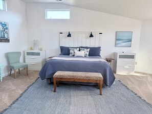 Ein Schlafzimmer mit einem Bett, zwei Nachttischen, einem Sessel, einer Bank und einem Fenster.
