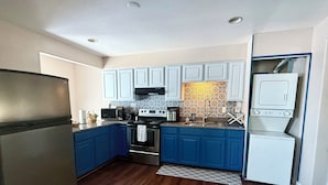 Una cocina compacta con armarios blancos, un refrigerador de acero inoxidable, un microondas, una estufa y un lavavajillas.