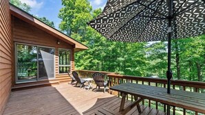 A wooden deck with outdoor furniture, including a table and chairs, and a large umbrella providing shade.