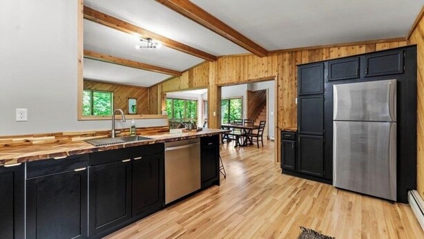 A modern kitchen with wooden beams, black cabinets, and a stainless steel refrigerator.