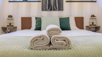 Un lit bien fait, avec des serviettes enroulées au centre, une couvre-lit à rayures vertes et blanches, et une peinture abstraite moderne accrochée au-dessus du lit.