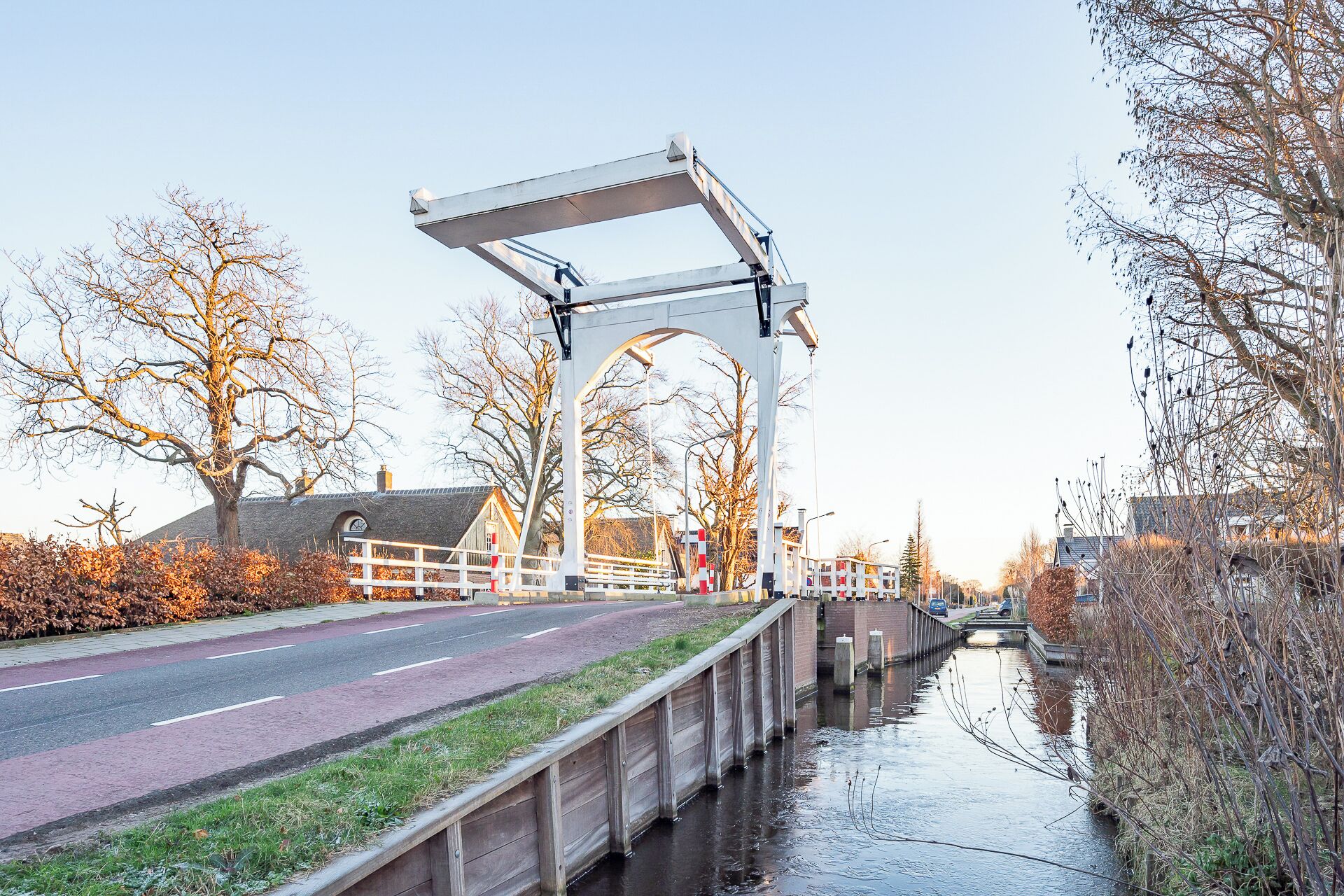 Un pont piétonnier enjambant un canal, avec une route de chaque côté, entouré d’arbres et de bâtiments.