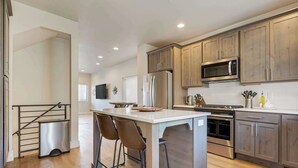 A modern kitchen with wooden cabinets, stainless steel appliances, and a central island with bar stools.