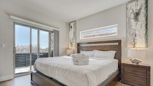 A modern bedroom with a large bed, a wooden headboard, and a nightstand with a lamp.