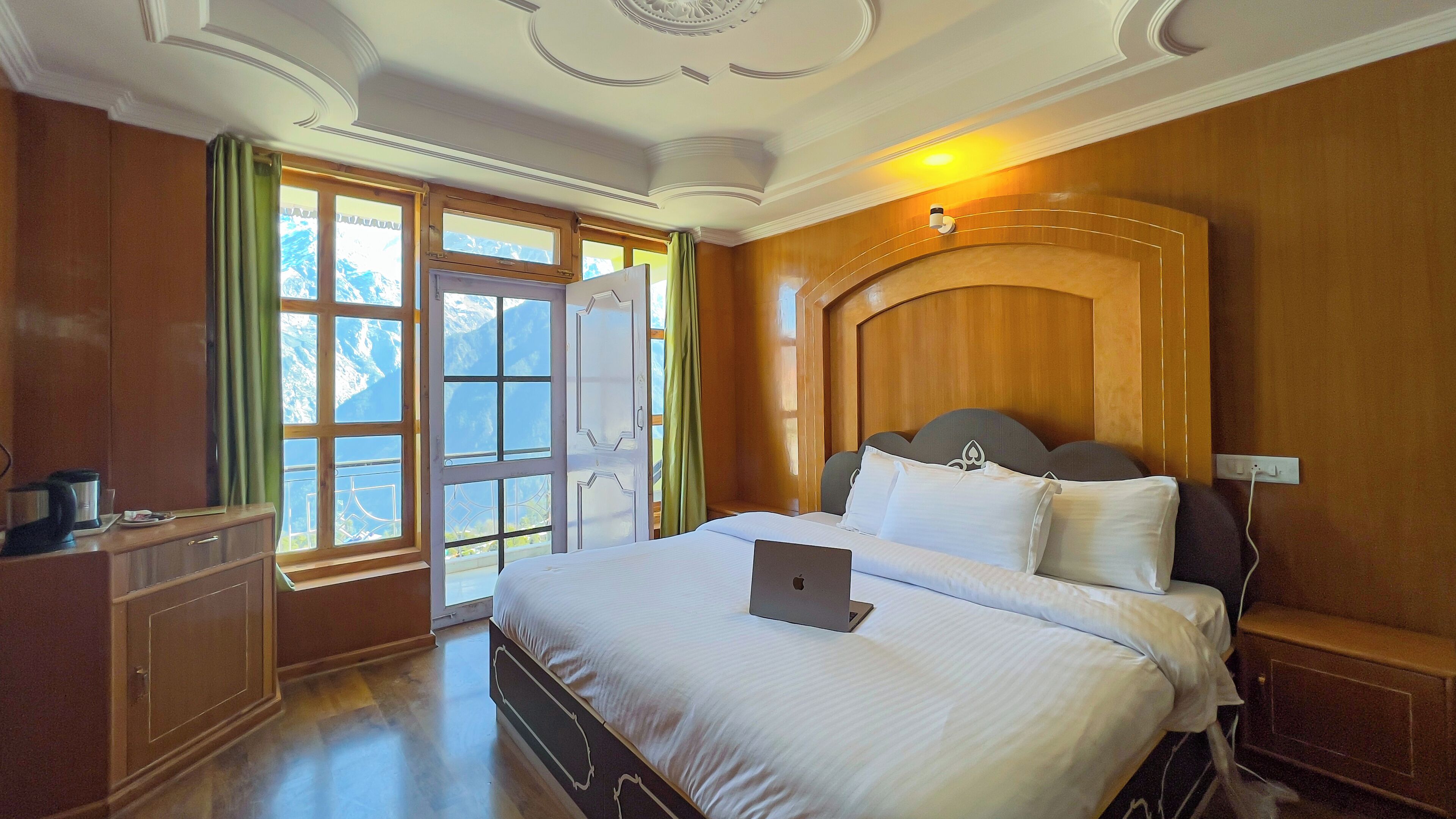 Ein Hotelzimmer mit einem großen Bett, einem Schreibtisch mit einem Laptop, Holzvertäfelung und Blick auf Berge durch die Fenster.