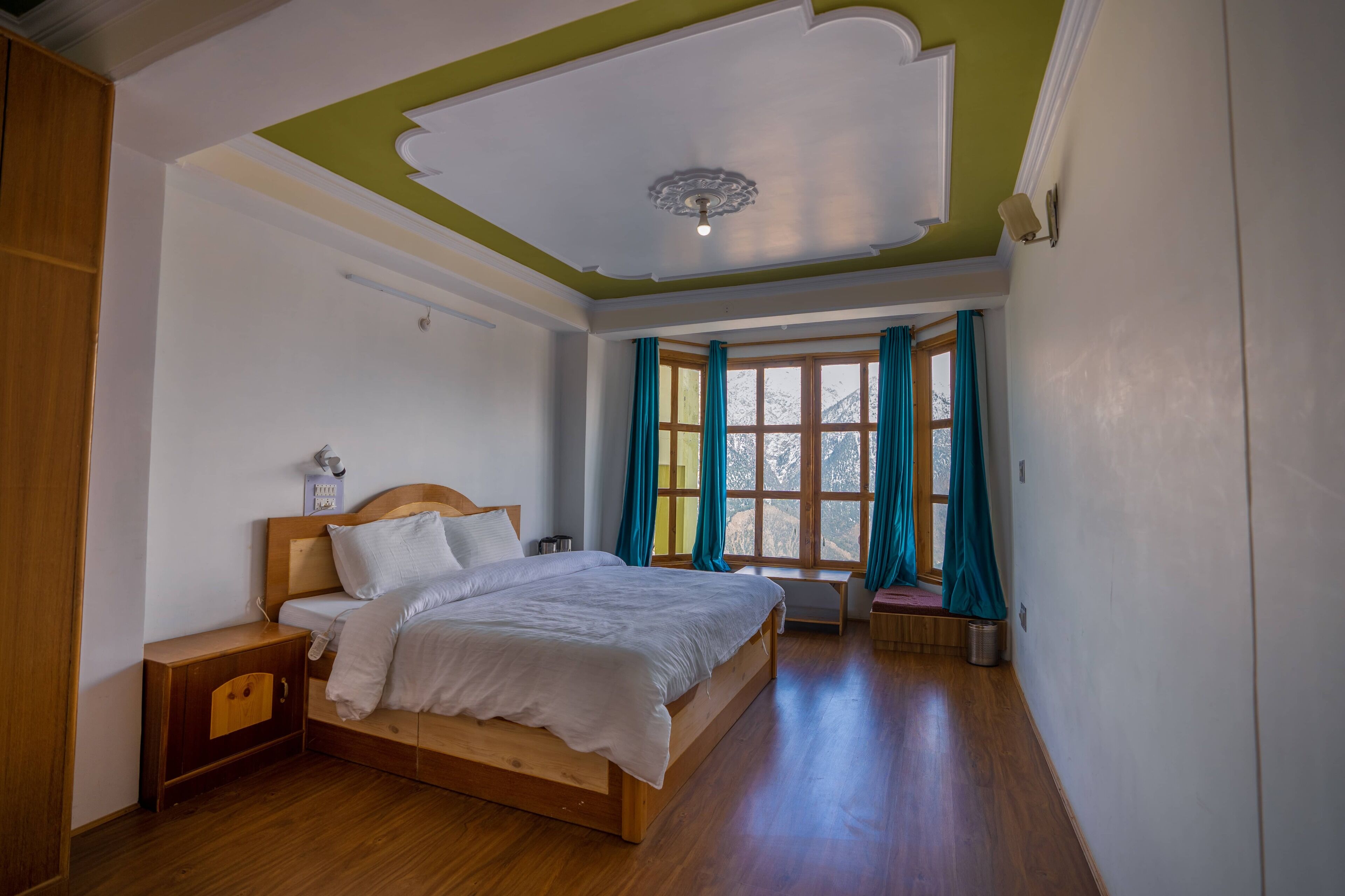 A bedroom with a wooden bed, a nightstand, a bench, and a window with curtains.