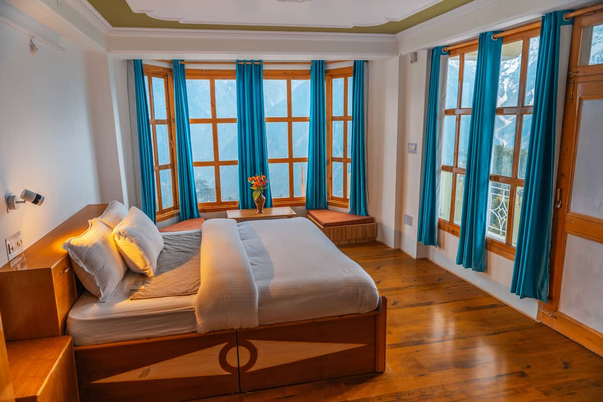 Une chambre à coucher avec un lit en bois, une table de chevet, une fenêtre avec des rideaux et une vue sur les montagnes.