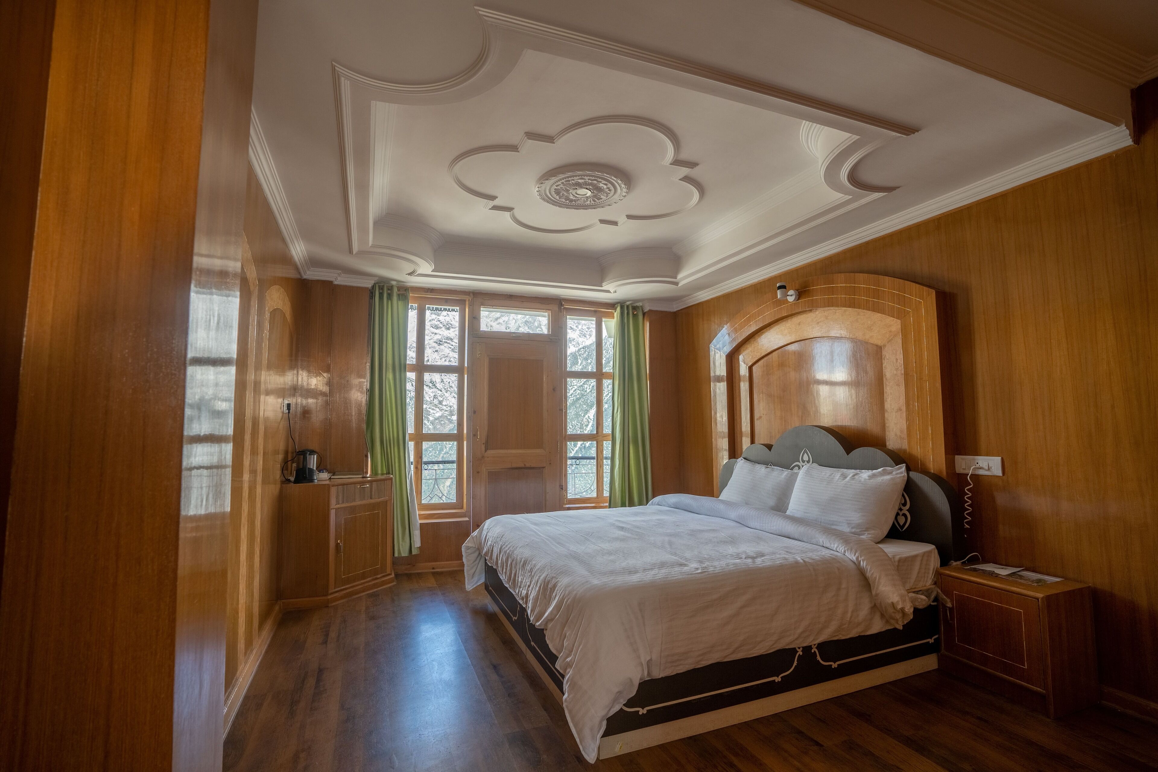 A bedroom with a wooden floor, a bed with white bedding, a nightstand, and a wooden headboard.