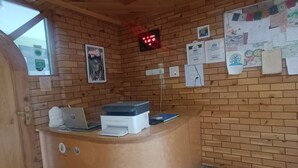 Zona de recepción con mostrador de madera, un reloj digital y un tablón de anuncios con avisos y fotografías.
