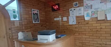 A reception area with a wooden reception desk, a digital clock, and a bulletin board with various notices and photos.