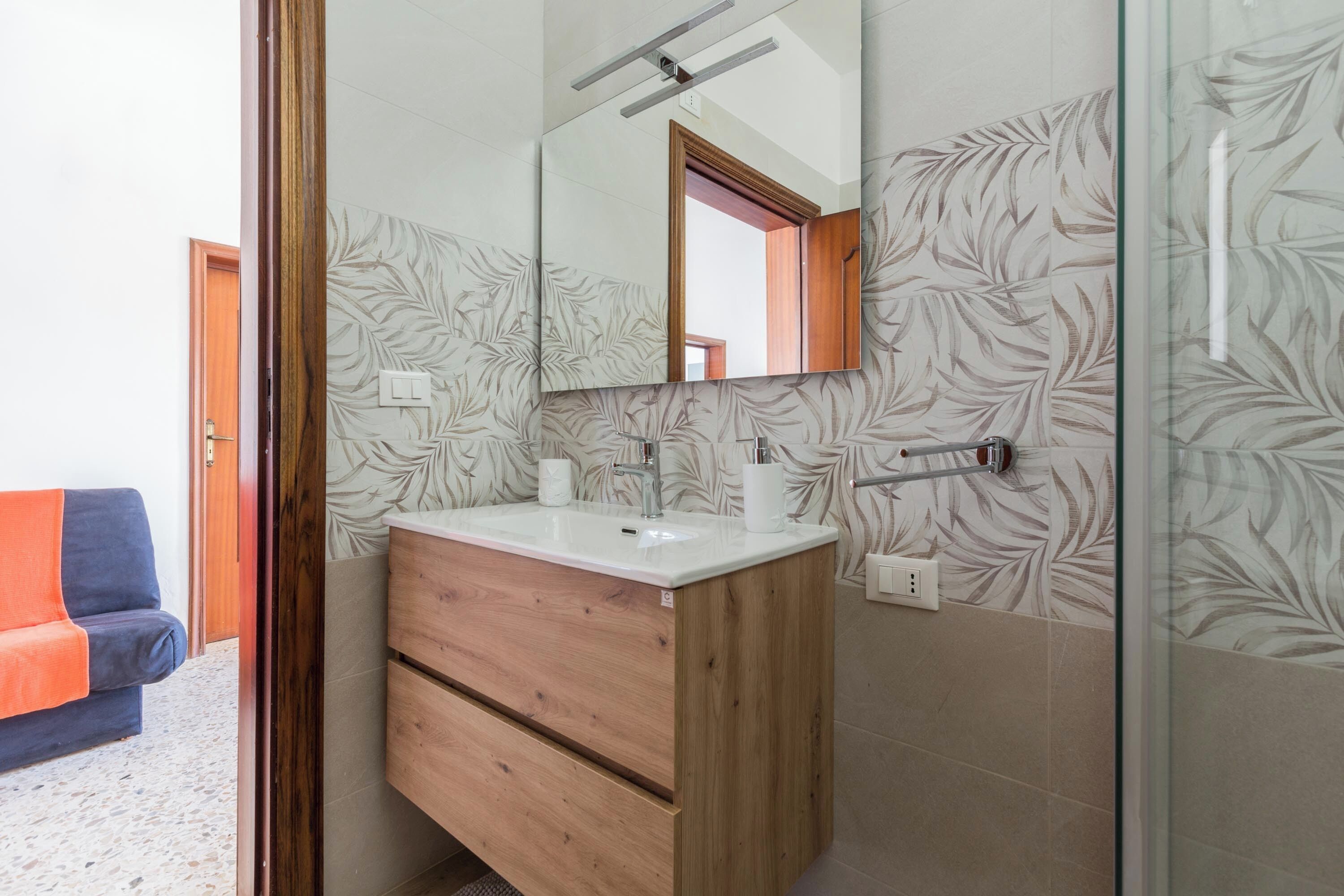 Een badkamer met een houten wastafelmeubel, een spiegel en een douchehoek.