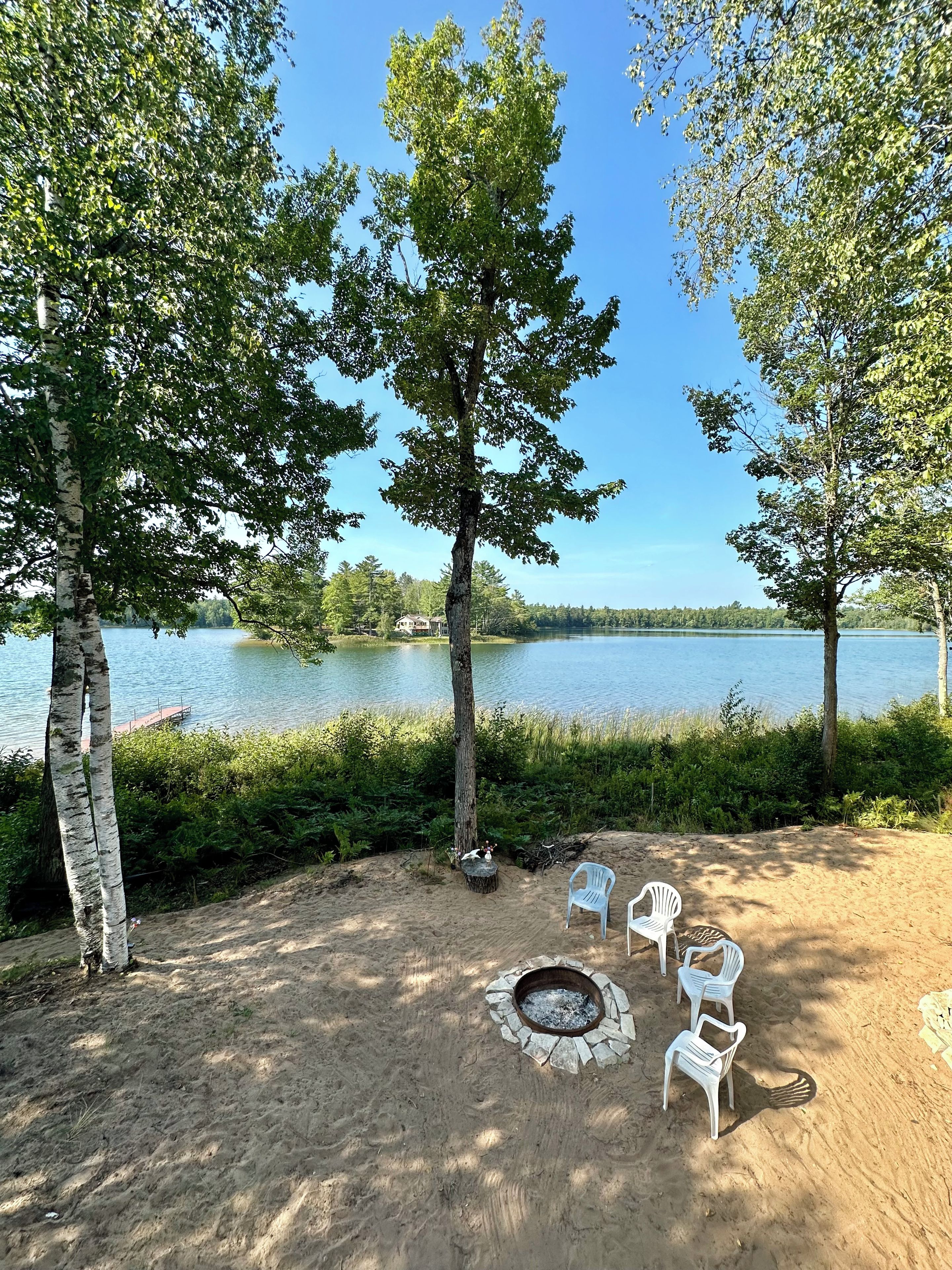 A lakeside outdoor seating area with a fire pit and white plastic chairs.