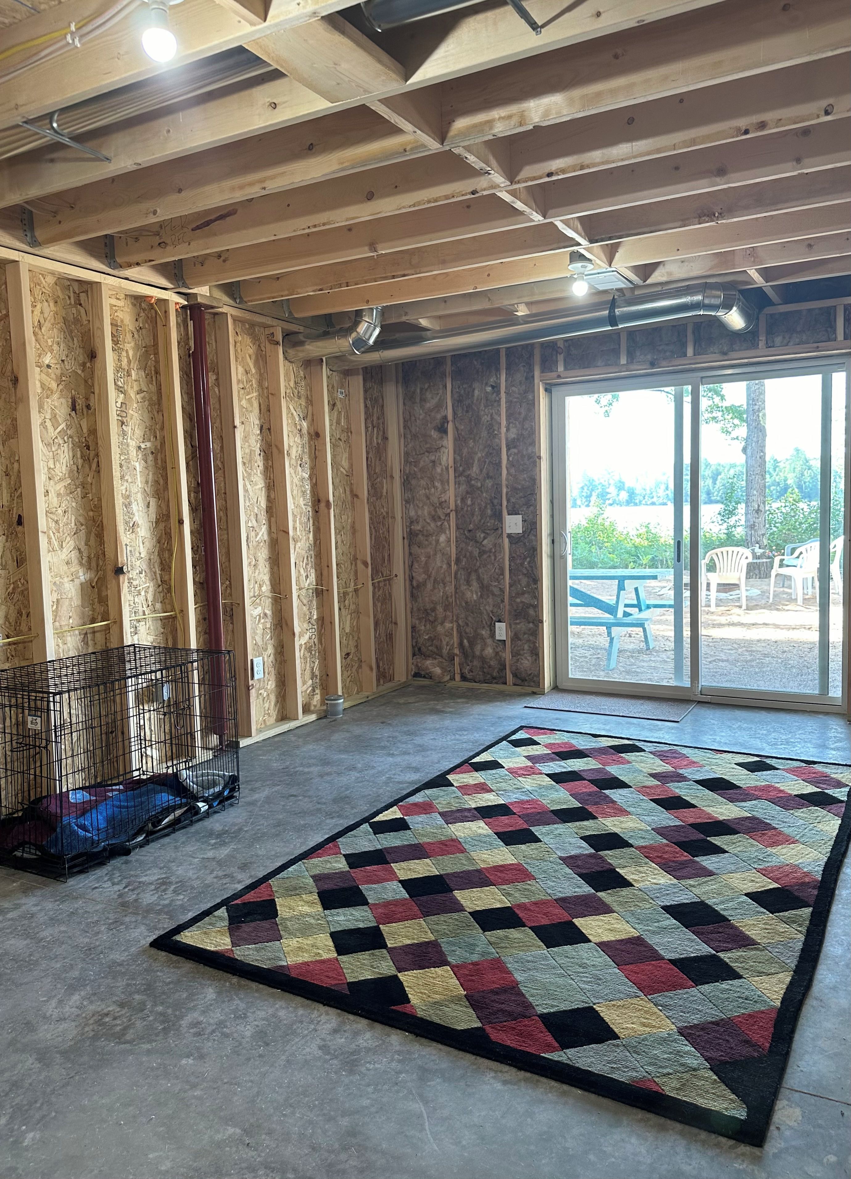 A room with exposed wooden beams, a large window, and a colorful rug.