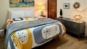 A bedroom with a bed, a nightstand, a lamp, a wall-mounted mirror, and a painting. - Pointview Cottage *A/C* overlooking Crooked Lake (Manistique)