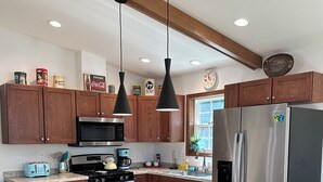 A modern kitchen with wooden cabinets, stainless steel appliances, and a central island with bar stools. - Pointview Cottage *A/C* overlooking Crooked Lake (Manistique)