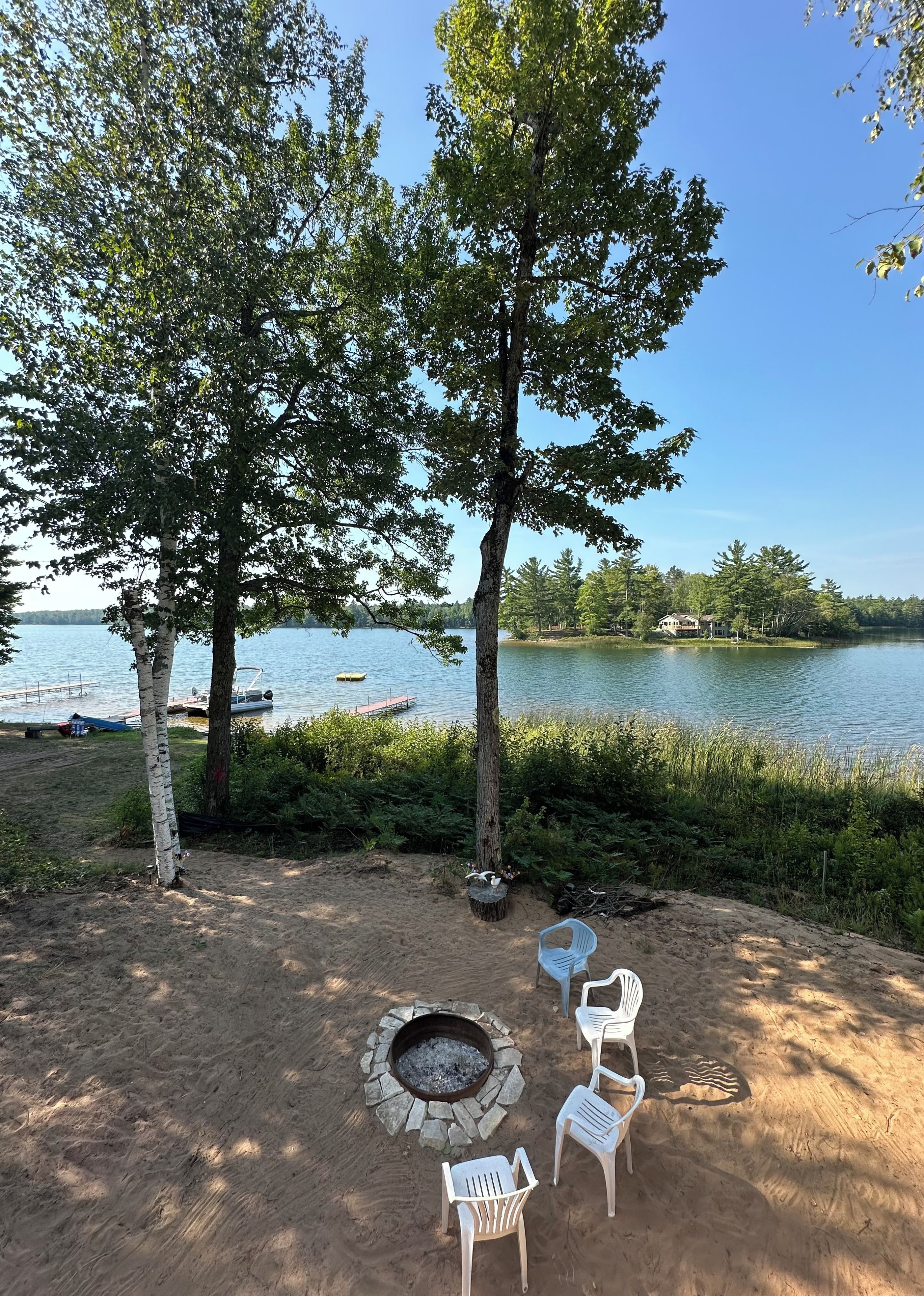 A lakeside outdoor seating area with a fire pit and white plastic chairs.