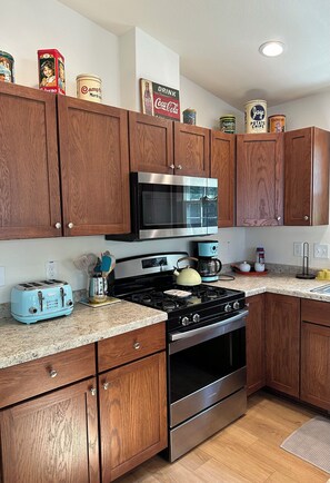 A modern kitchen with wooden cabinets, stainless steel appliances, and a granite countertop. - Pointview Cottage *A/C* overlooking Crooked Lake (Manistique)