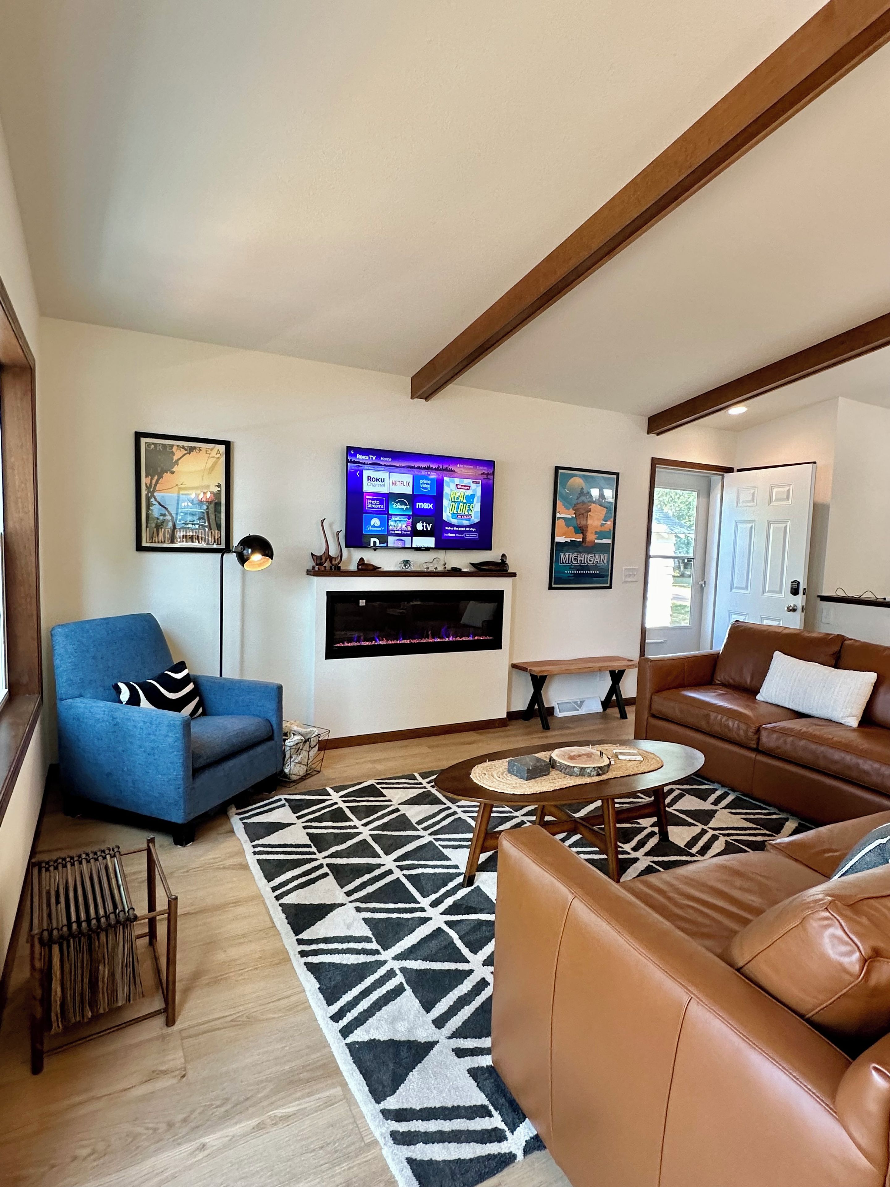 A living room with a blue armchair, a brown leather sofa, a fireplace, a television, and a patterned rug.