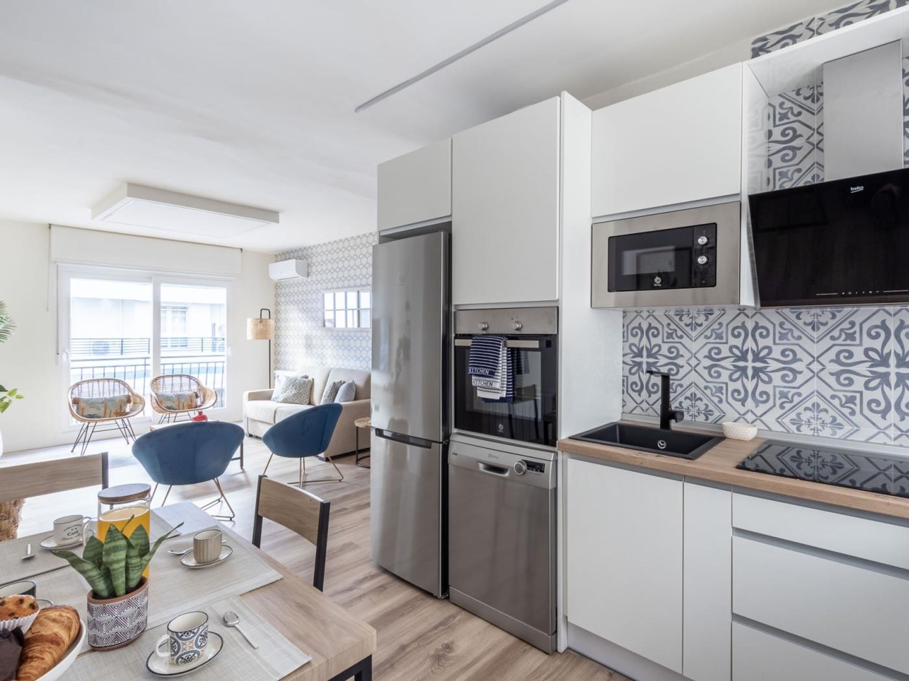A modern kitchen with stainless steel appliances, a dining area with a table and chairs, and a balcony with a view.