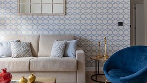 En stue med en beige sofa, mønstrede puder, en blå lænestol og et lille rundt bord med stearinlys.