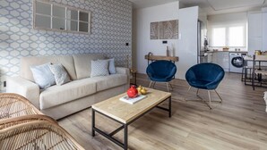 En moderne stue med en sofa, to lænestole, et sofabord og et køkken i baggrunden.