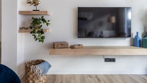 En moderne stue med et fladskærms-tv monteret på væggen, træflydende hylder, en vævet kurv og en blå stol.
