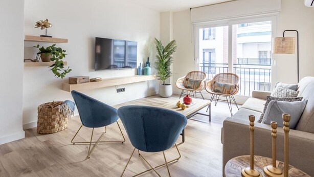 En moderne stue med et fladskærms-tv, blå stole, en sofa og en balkon med udsigt.