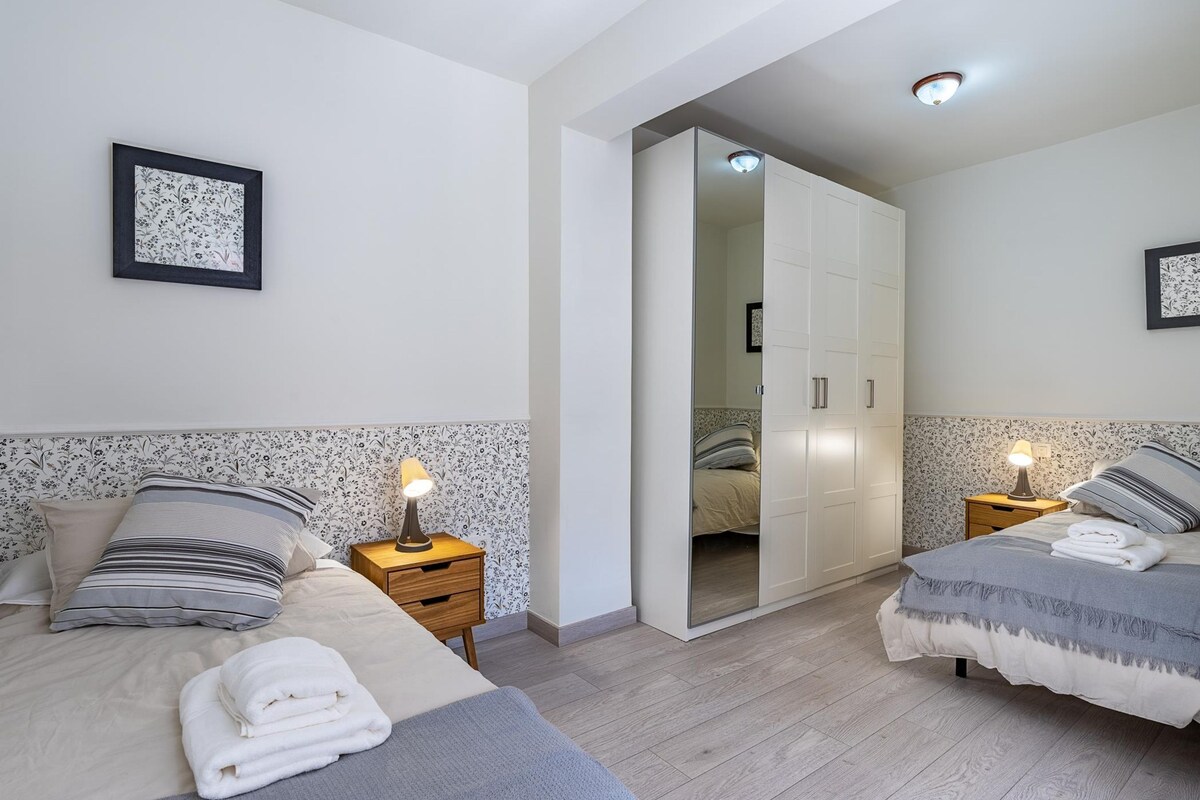 A modern hotel room with two beds, a wardrobe, and a bathroom visible through an open door.
