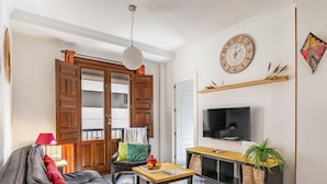A modern living room with a leather sofa, wooden door, TV, and a clock on the wall. - Luxury Suite Ancha de la Virgen (Granada)