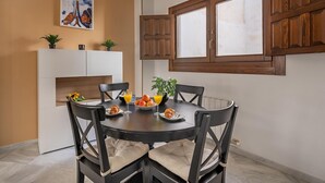 A dining area with a round table, four chairs, a white fireplace, and a large window with wooden shutters. - Luxury Suite Ancha de la Virgen (Granada)
