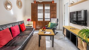 A modern living room with a black leather sofa, a wooden coffee table, a TV, and a large wooden door. - Luxury Suite Ancha de la Virgen (Granada)