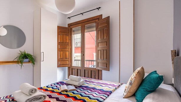 A bedroom with a bed, a window with wooden shutters, a potted plant, and a mirror on the wall. - Luxury Suite Ancha de la Virgen (Granada)