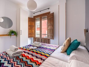 Un dormitorio con cama, una ventana con contraventanas de madera, una planta en maceta y un espejo en la pared.