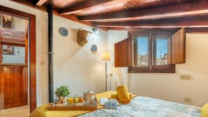 Ein Schlafzimmer mit einem Bett, einem Fenster, einer Lampe und einem kleinen Tisch mit Pflanze und Buch.