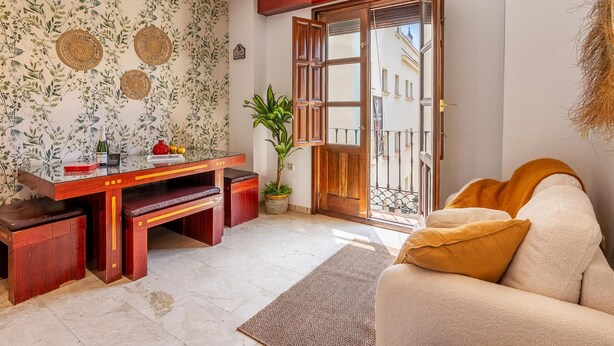 Ein Wohnzimmer mit einem Holztisch, einer Couch, einem Blumentopf und einer Tür, die auf einen Balkon im Freien führt.