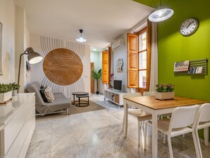 Una sala de estar moderna con un sofá gris, un adorno circular en la pared, una mesa de comedor con sillas y una pared de acento verde.