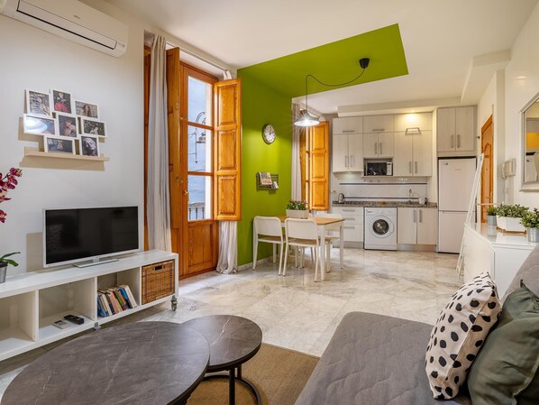 A compact living space with a TV, bookshelf, dining area, and kitchenette. - Luxury Suites San Mat as (Granada)