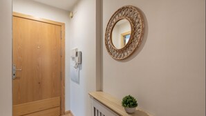 A hallway with a wooden door, a wall-mounted mirror, and a small plant on a console table. - Luxury Suite Campo del Pr Ncipe (Granada)