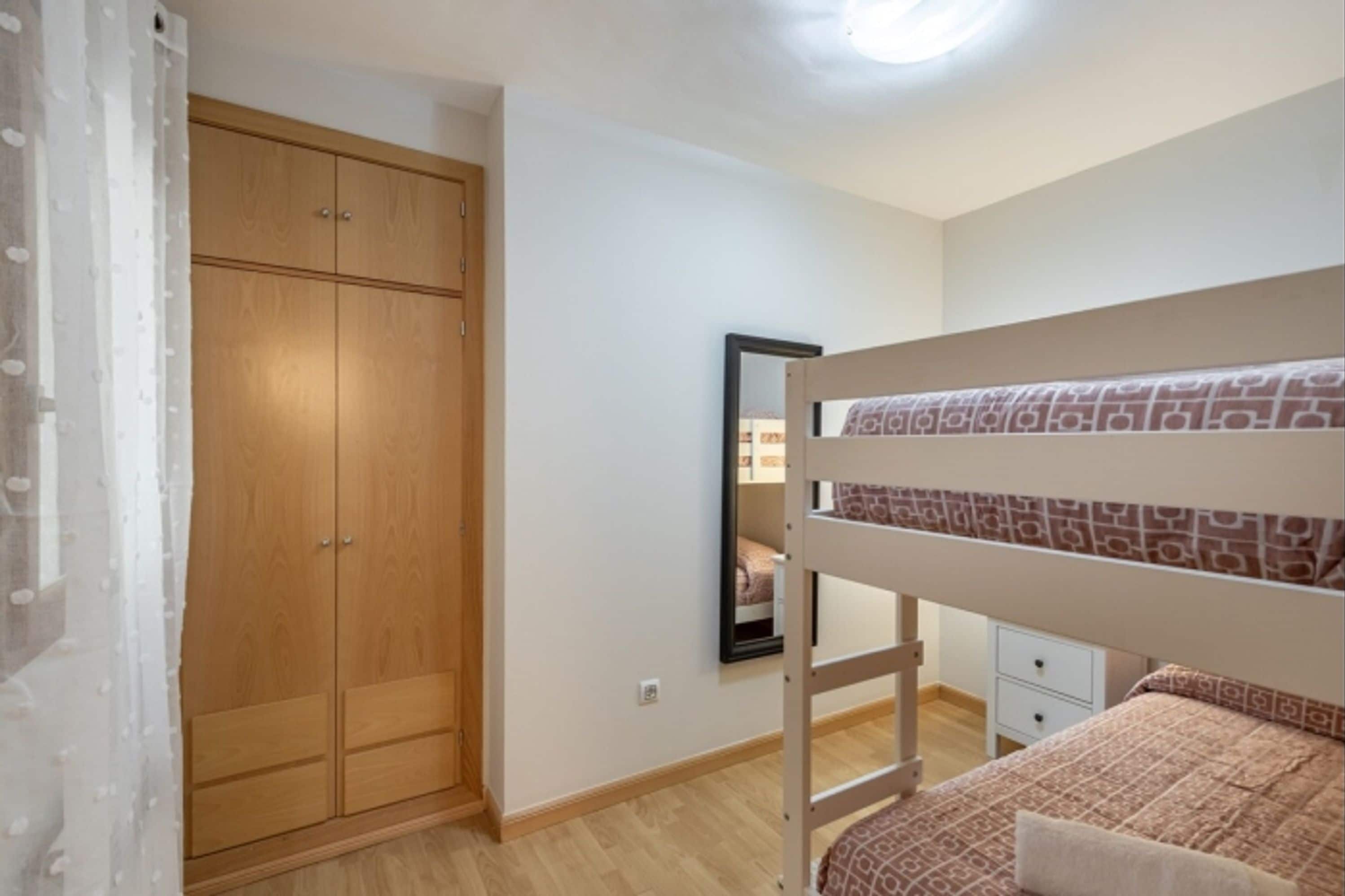 Une chambre à coucher avec un lit superposé, une armoire en bois, un miroir et une petite table de chevet.