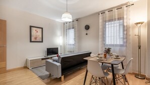 A modern living room with a sofa, a dining table with chairs, a TV, and a floor lamp. - Luxury Suite Campo del Pr Ncipe (Granada)