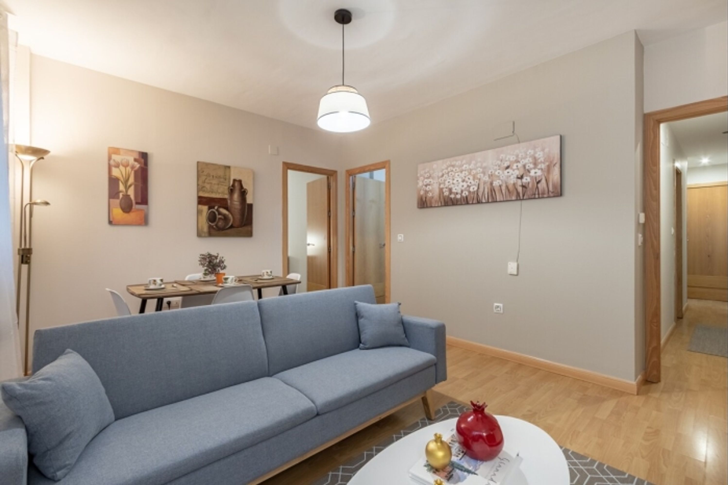 A living room with a blue sofa, a dining table, and a painting on the wall.