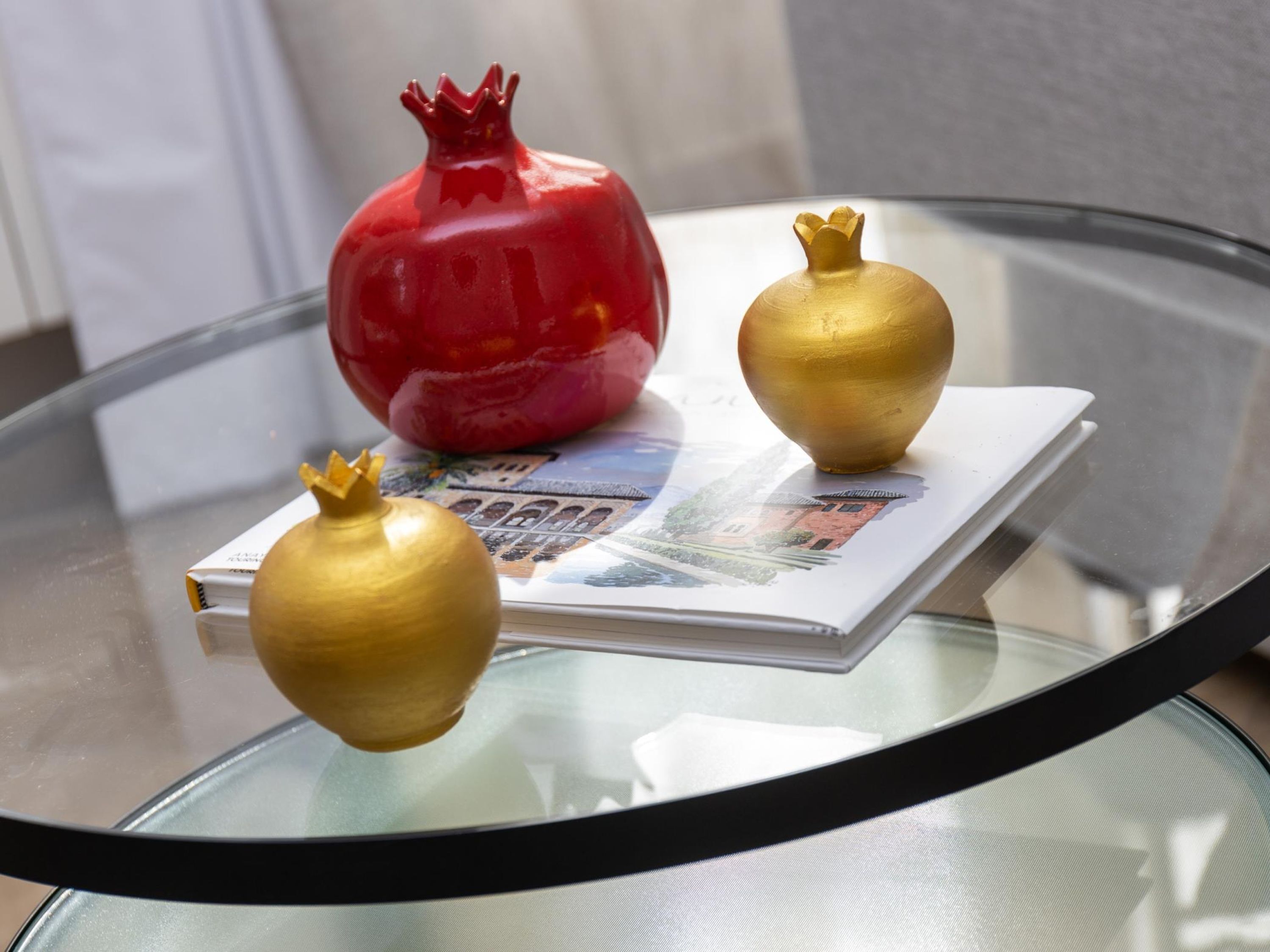 Een glazen tafel met drie granaatappels, één rood en twee gouden, op een tijdschrift.