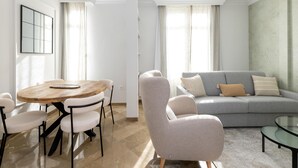 Een moderne woonkamer met een ronde houten tafel, een grijze bank en een glazen bijzettafeltje.