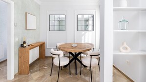 Een moderne eethoek met een ronde houten tafel, vier stoelen, een houten bank en een fles wijn aan de linkerkant.